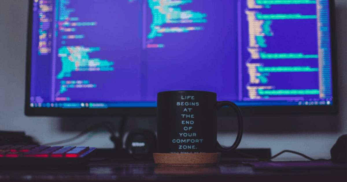 A coffee cup in front of a computer with ruby on rails and javascript code
